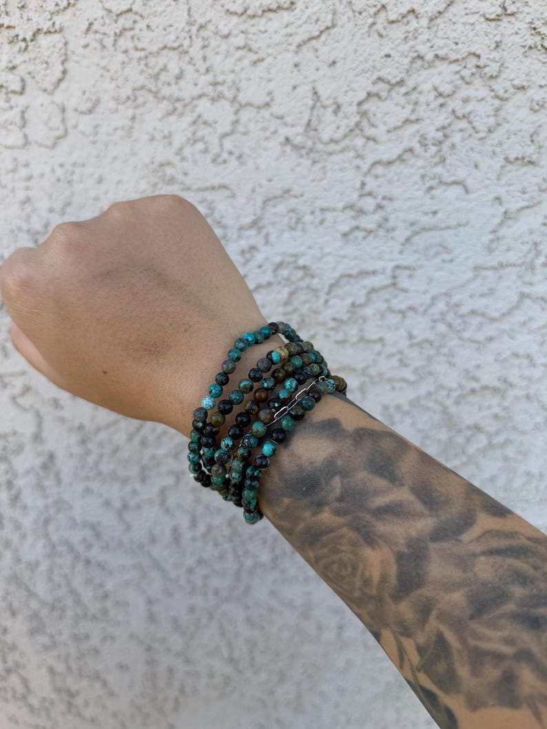 May include: A stack of turquoise and brown beaded bracelets on a person's wrist.