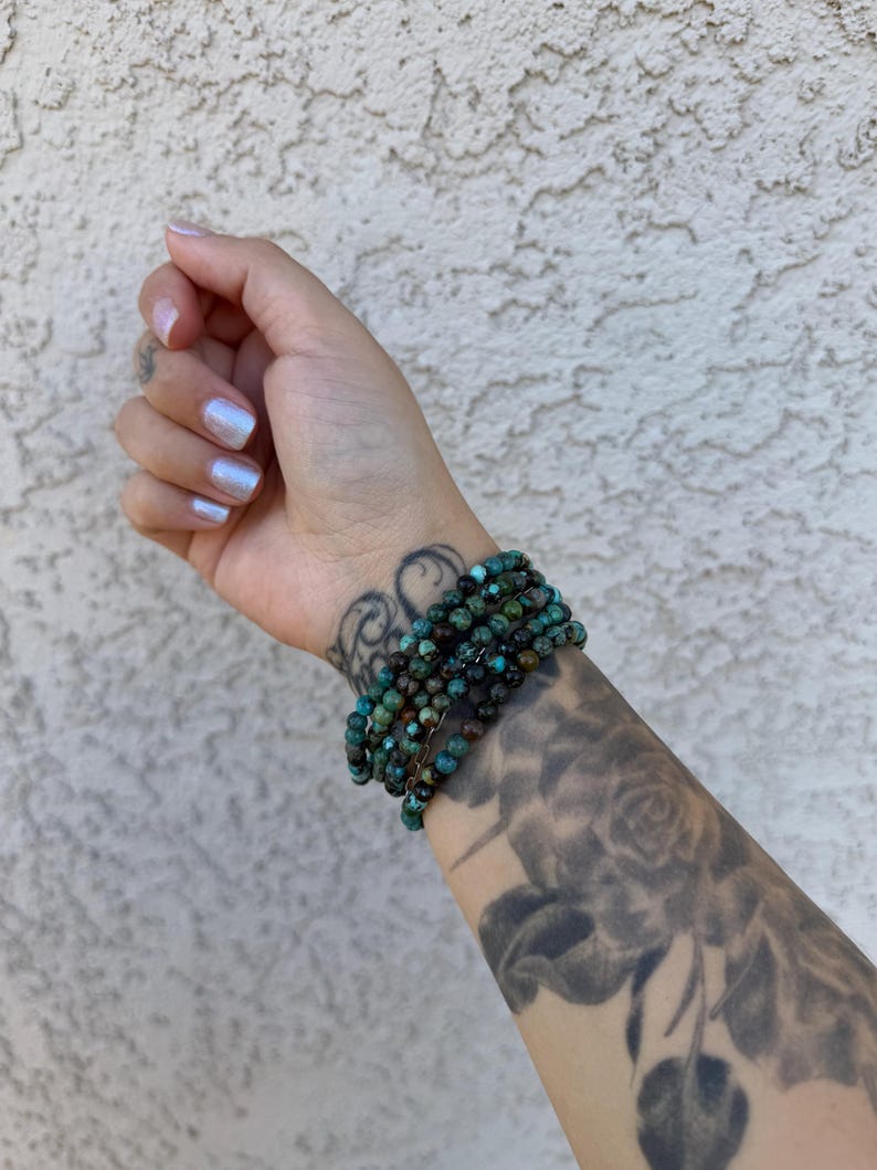 May include: A turquoise gemstone bracelet with multiple strands of small beads. The bracelet is worn on a person's wrist.