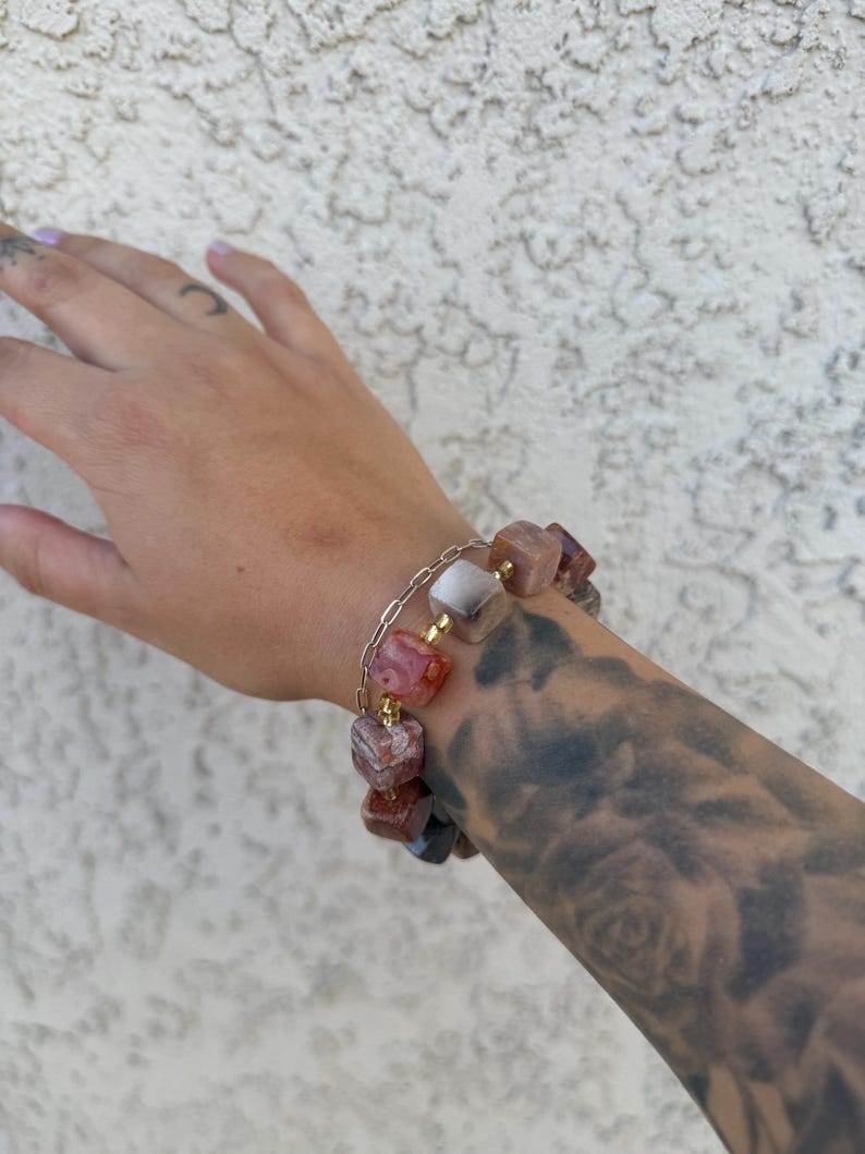 K&ouml;nnte beinhalten: Ein Armband mit einer goldenen Kette und quadratischen roten, wei&szlig;en und braunen Achatperlen.