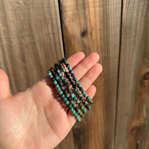 May include: A stack of five turquoise and black beaded bracelets. The bracelets are made of small, round beads and are stacked on top of each other.