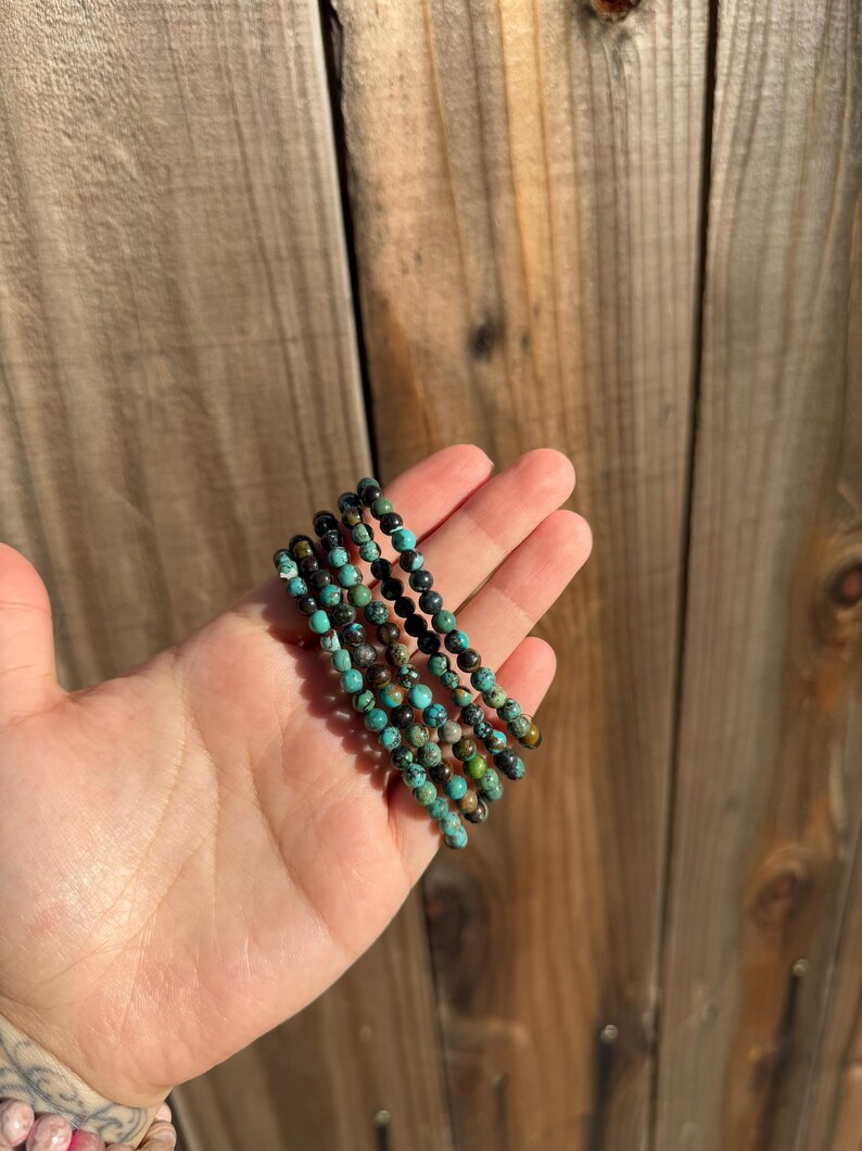 May include: A stack of five turquoise and black beaded bracelets. The bracelets are made of small, round beads and are stacked on top of each other.