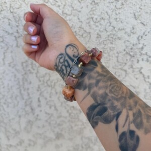 K&ouml;nnte beinhalten: Ein Armband aus kleinen, quadratischen Steinen in den Farben Rosa, Orange und Braun. Die Steine sind auf einer silbernen Kette aufgef&auml;delt.