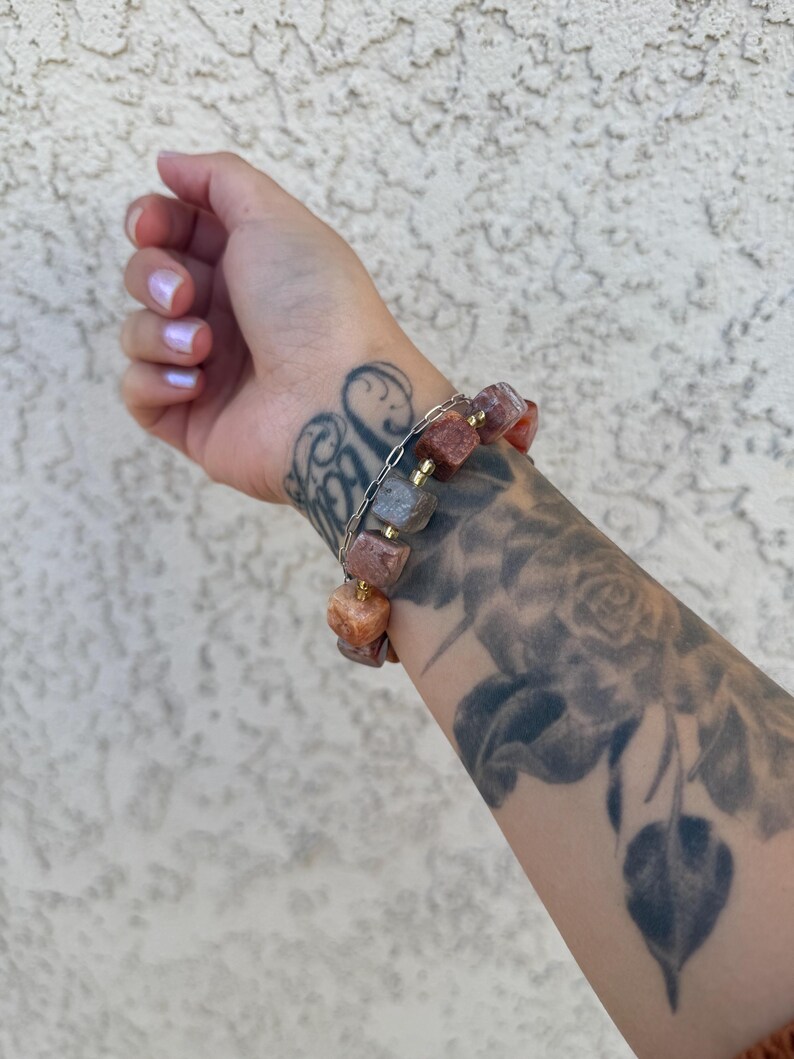 K&ouml;nnte beinhalten: Ein Armband aus kleinen, quadratischen Steinen in den Farben Rosa, Orange und Braun. Die Steine sind auf einer silbernen Kette aufgef&auml;delt.