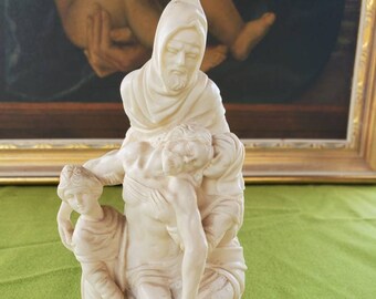 May include: A white ceramic sculpture depicting the Pietà, a scene of Mary holding the body of Jesus after his crucifixion. The sculpture is detailed and shows the sorrow and grief of the figures.