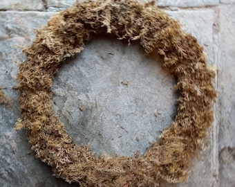May include: A brown, dried moss wreath, circular in shape, against a grey concrete background.