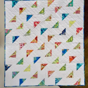 May include: A white quilt with a repeating pattern of colorful triangles. The triangles are filled with various floral and patterned fabrics in shades of blue, green, red, and orange. The quilt has a blue border and is machine quilted.