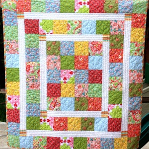 May include: A patchwork quilt featuring a range of colourful squares, including red, yellow, green, blue, and pink. The quilt is made with a white border and a white backing.