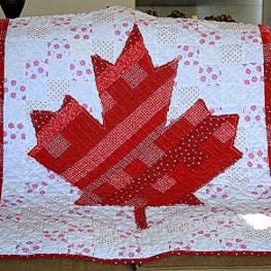 May include: A red and white quilt with a maple leaf design in the centre, representing the Canadian flag. The quilt has a patchwork pattern with red squares on the sides and a white background with red polka dots.