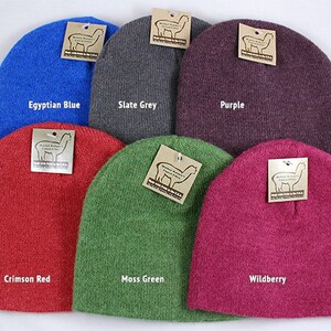 May include: A collection of six beanies in various colors: Egyptian Blue, Slate Grey, Purple, Crimson Red, Moss Green, and Wildberry. Each beanie has a tag with a logo. The beanies are made of a soft, textured material.