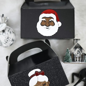 May include: Two black favour boxes with glitter. One box features a black Santa Claus with a red hat and white beard. The other box features a black woman with a red bow in her hair and glasses.