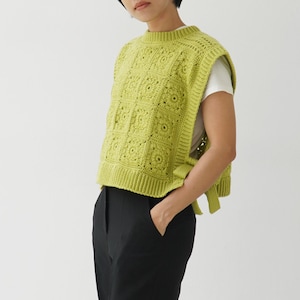 May include: A lime green crochet vest with a square pattern and a tie at the back. The vest is worn over a white t-shirt and black pants.