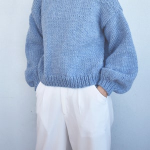 May include: A light blue knitted sweater with long sleeves and a round neckline.