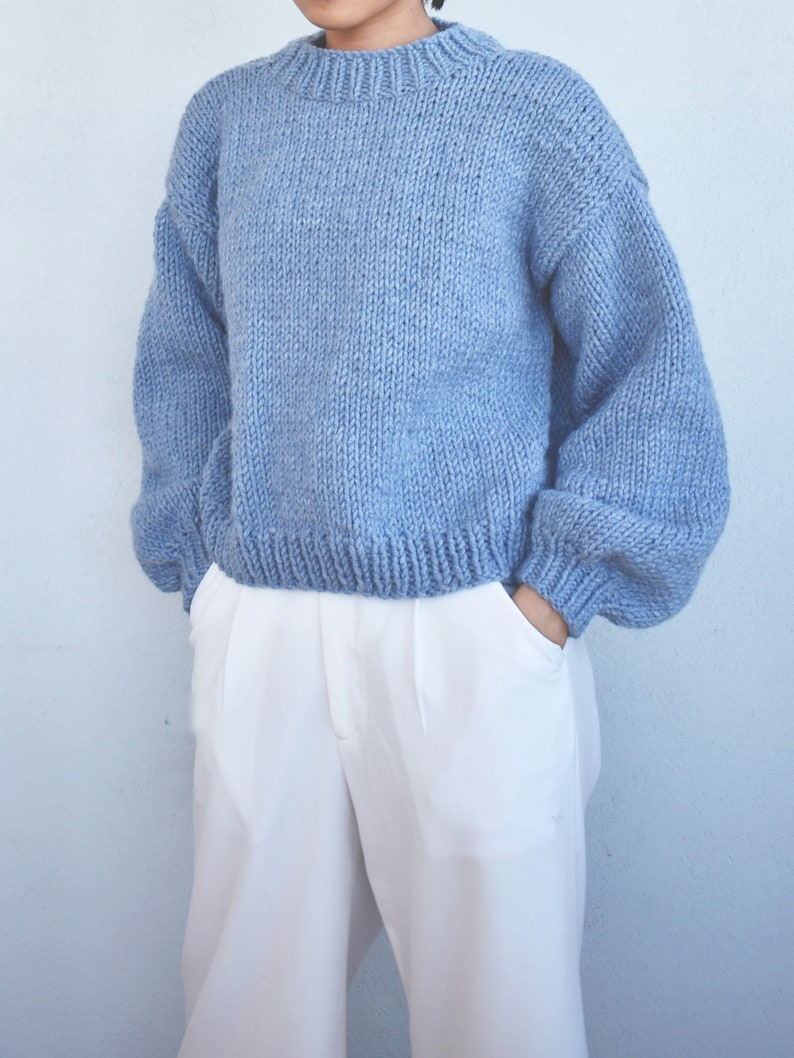 May include: A light blue knitted sweater with long sleeves and a round neckline.