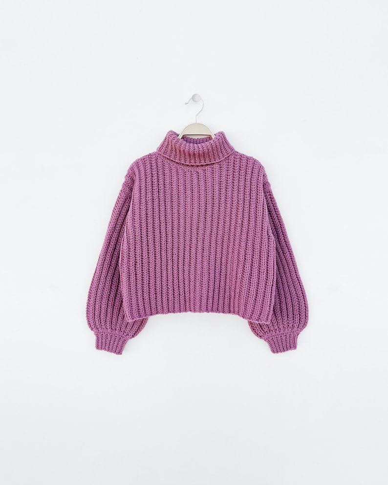 May include: A purple turtleneck sweater with a ribbed knit texture. The sweater has long sleeves and a relaxed fit.