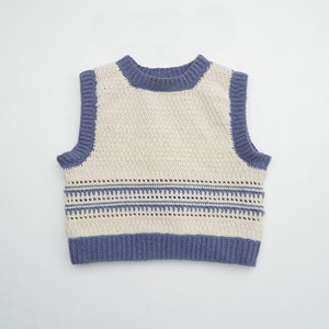 Pode incluir: Um colete de crochê sem mangas, em esquema de cores branco e azul. O colete tem um decote redondo largo e um padrão de crochê com uma borda azul.
