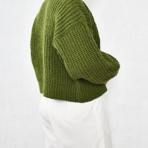 May include: A green knitted sweater with long sleeves and a relaxed fit.