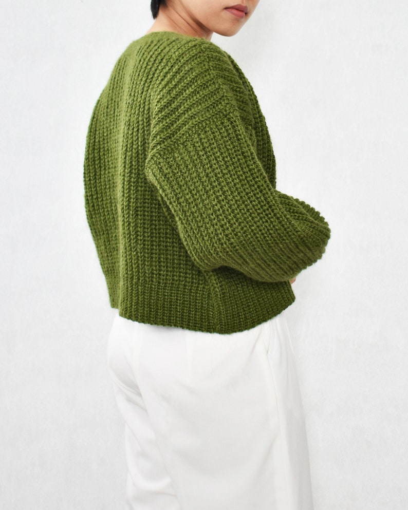 May include: A green knitted sweater with long sleeves and a relaxed fit.
