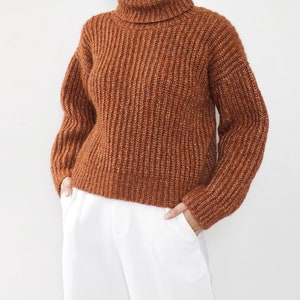 May include: A brown turtleneck sweater with a ribbed knit texture. The sweater has a relaxed fit and long sleeves.