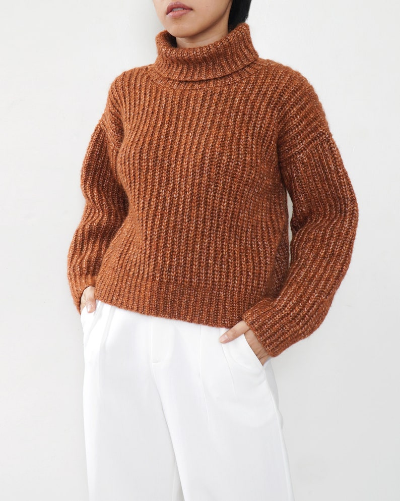 May include: A brown turtleneck sweater with a ribbed knit texture. The sweater has a relaxed fit and long sleeves.