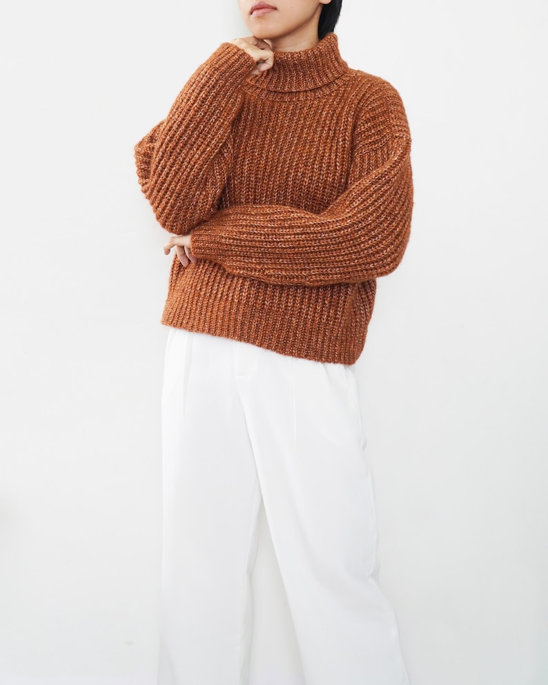 May include: A brown turtleneck sweater with a chunky knit texture. The sweater has a relaxed fit and is made of a soft, comfortable material.