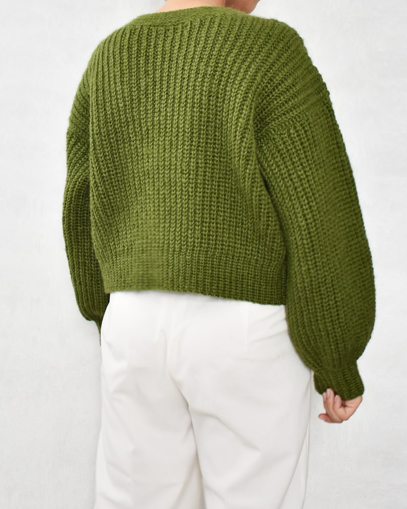May include: A green knitted cardigan with long sleeves and a ribbed texture.