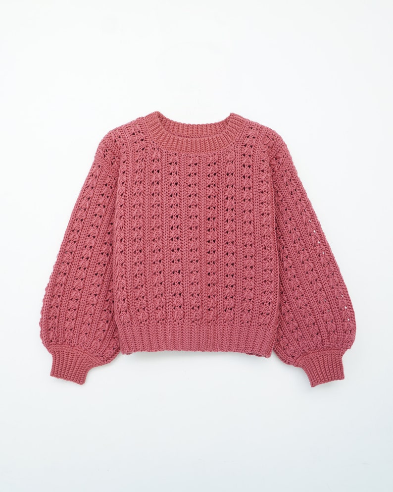 May include: A pink knitted sweater with a loose fit and long sleeves. The sweater has a delicate openwork pattern.