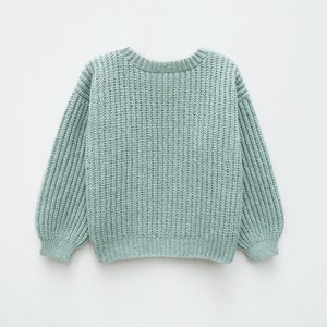 May include: A light sage green long-sleeve sweater featuring a chunky ribbed knit texture, a rounded crew neckline, and ribbed cuffs at the wrists and hem. The garment is constructed with a thick, vertical knit pattern throughout.