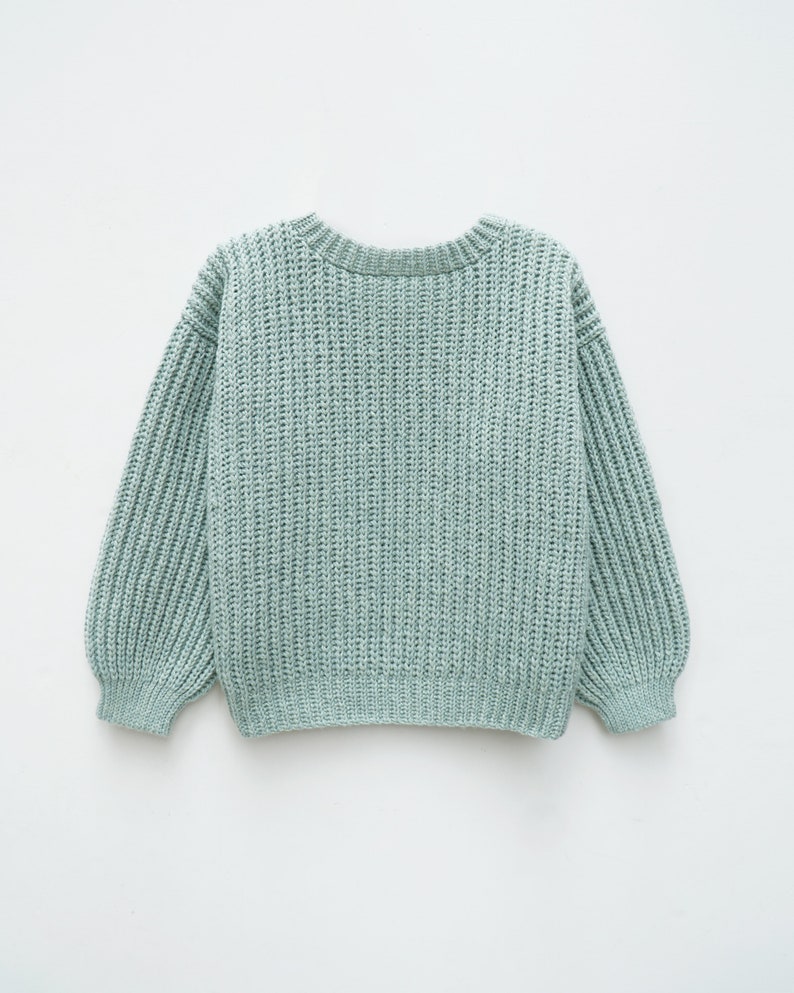 May include: A light sage green long-sleeve sweater featuring a chunky ribbed knit texture, a rounded crew neckline, and ribbed cuffs at the wrists and hem. The garment is constructed with a thick, vertical knit pattern throughout.