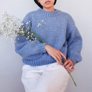 May include: A light blue knitted sweater with a round neckline and long sleeves. The sweater is made of a soft, fluffy yarn and has a relaxed fit.