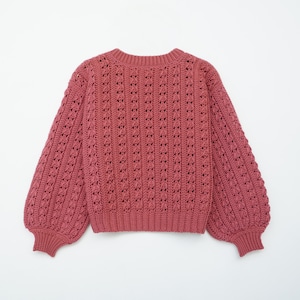 May include: A pink crocheted sweater with a loose fit and long sleeves. The sweater has a delicate openwork pattern.