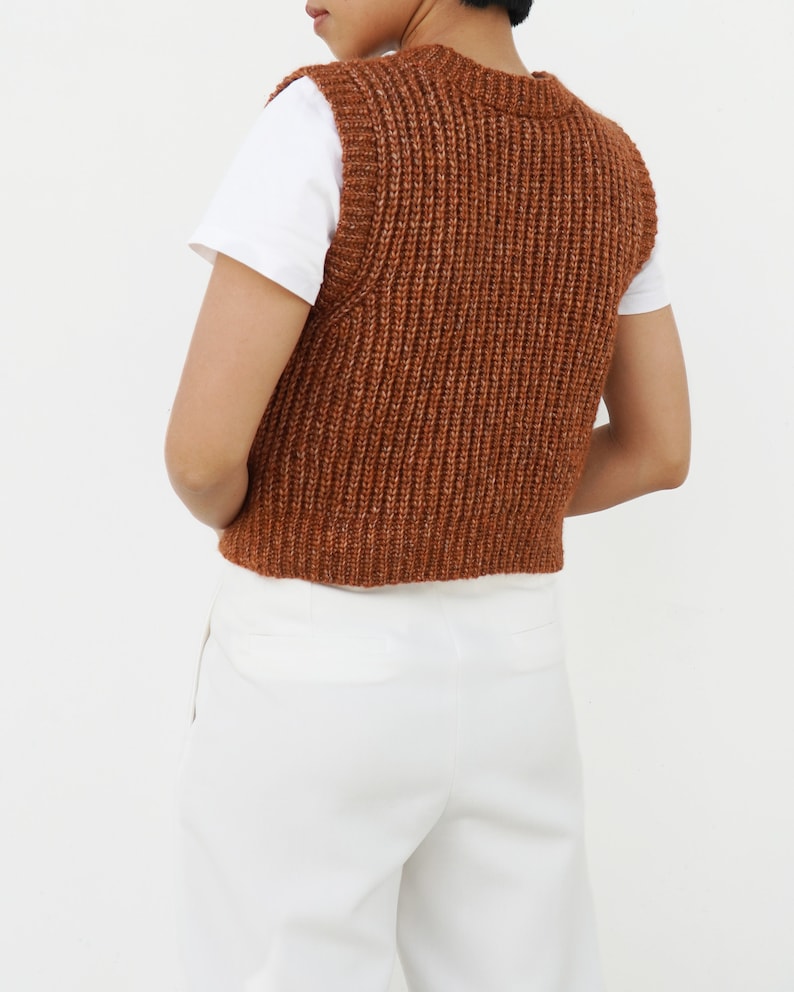 K&ouml;nnte beinhalten: Eine braune Strickweste mit gerippter Struktur. Die Weste ist &auml;rmellos und hat einen Rundhalsausschnitt.