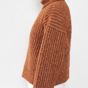 May include: A brown turtleneck sweater with a ribbed knit texture. The sweater has a slightly cropped length and long sleeves.
