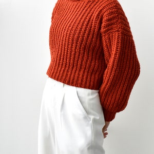 May include: A rust-colored chunky knit turtleneck sweater with long sleeves and a cropped length.