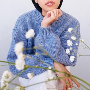 May include: A light blue knitted sweater with a relaxed fit and long sleeves. The sweater is made of a soft, comfortable material and has a slightly oversized look.