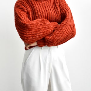May include: A rust-colored turtleneck sweater with a ribbed knit texture. The sweater is cropped and has a relaxed fit.