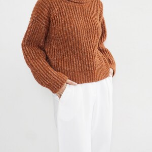 May include: A brown turtleneck sweater with a ribbed knit texture. The sweater is cropped and has a relaxed fit.