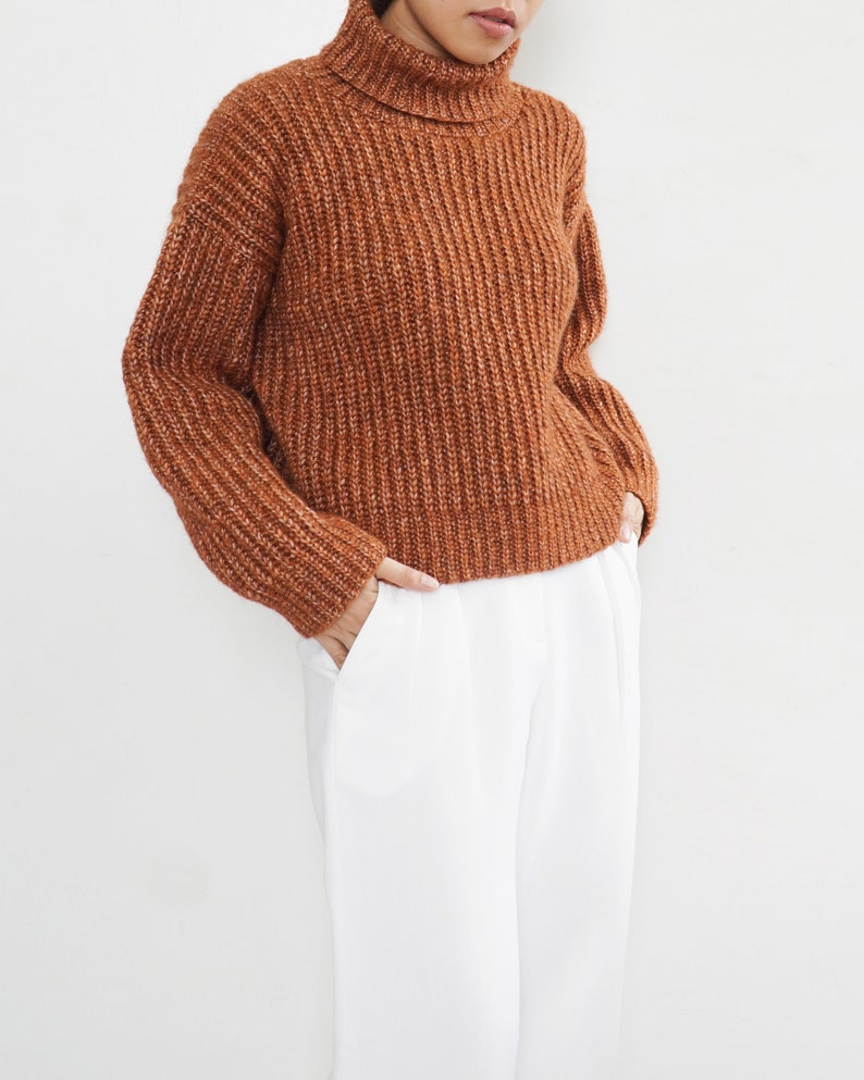 May include: A brown turtleneck sweater with a ribbed knit texture. The sweater is cropped and has a relaxed fit.