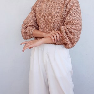 May include: A brown and white knit sweater with a round neckline and long sleeves. The sweater is cropped and has a loose fit.