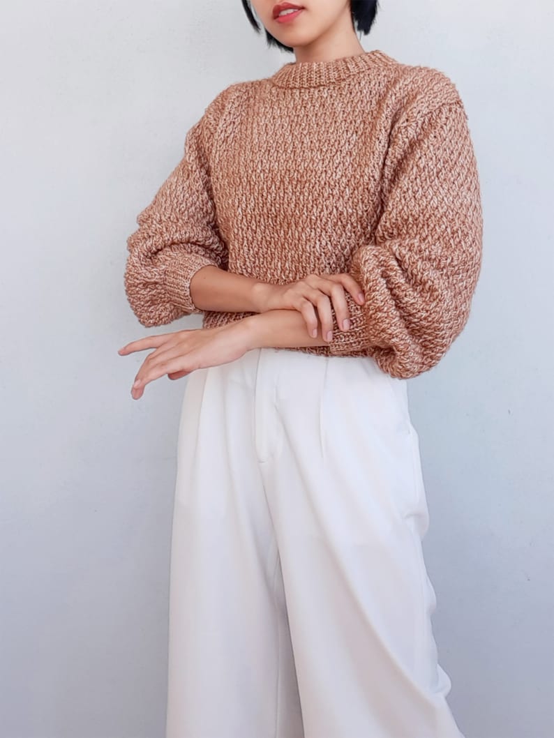 May include: A brown and white knit sweater with a round neckline and long sleeves. The sweater is cropped and has a loose fit.
