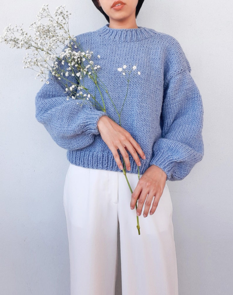 May include: A light blue knitted sweater with a round neckline and long sleeves. The sweater has a relaxed fit and is made of a soft, chunky yarn.