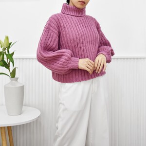May include: A pink, chunky knit turtleneck sweater with puffed sleeves.