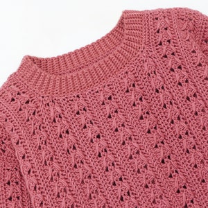 May include: A close-up of a pink crocheted sweater with a delicate openwork pattern.