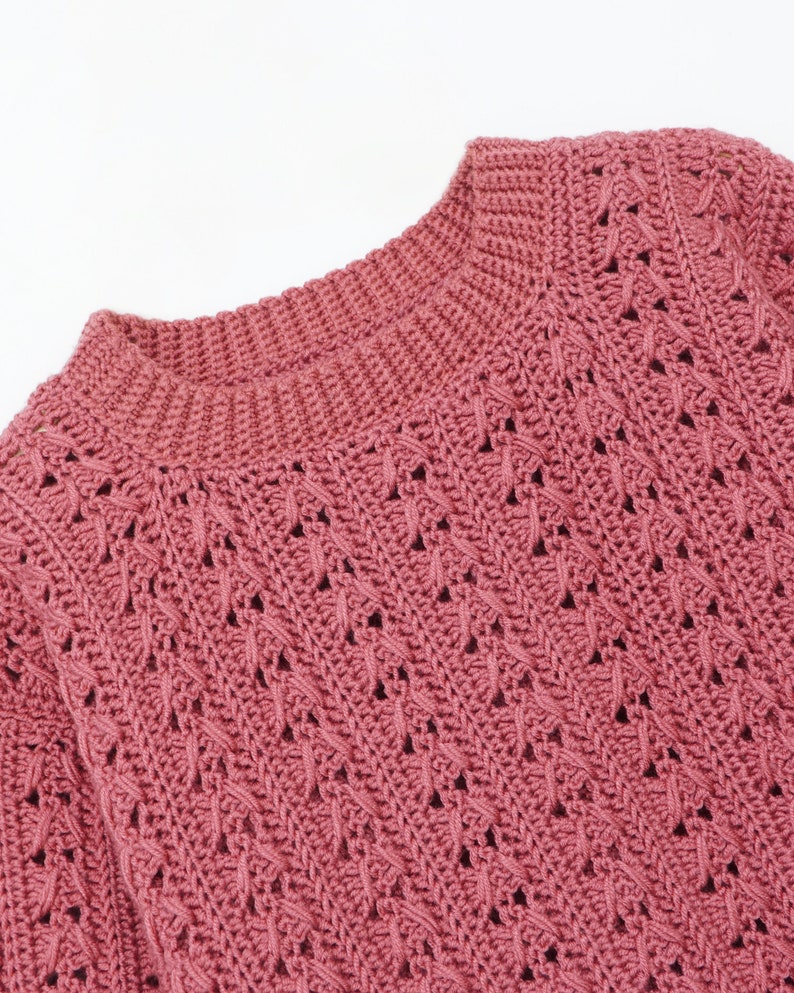 May include: A close-up of a pink crocheted sweater with a delicate openwork pattern.