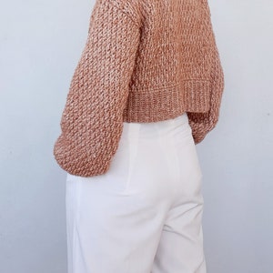May include: A brown cropped knitted sweater with a textured knit pattern. The sweater has long sleeves and a relaxed fit.
