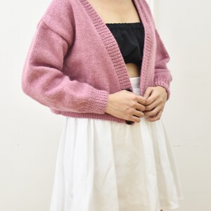 May include: A pink knitted cardigan with a single button closure. The cardigan has a V-neck and long sleeves.