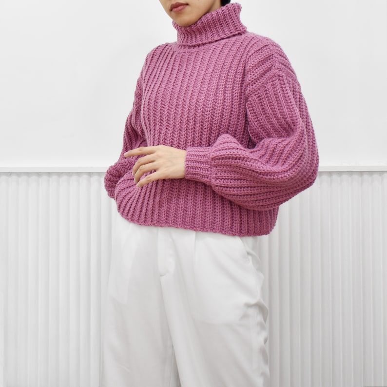 May include: A pink knitted turtleneck sweater with a ribbed texture and slightly puffed sleeves.