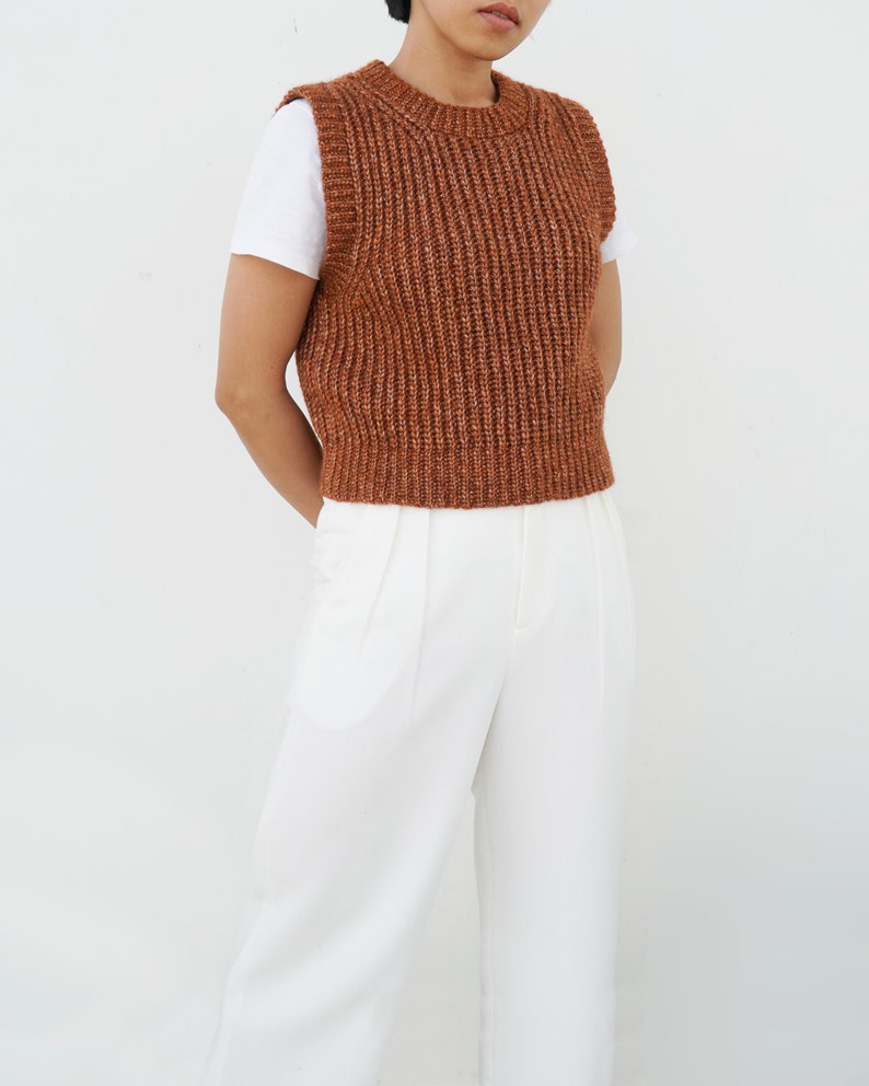 K&ouml;nnte beinhalten: Eine braune Strickweste mit gerippter Struktur. Die Weste hat einen runden Ausschnitt und ist &auml;rmellos.