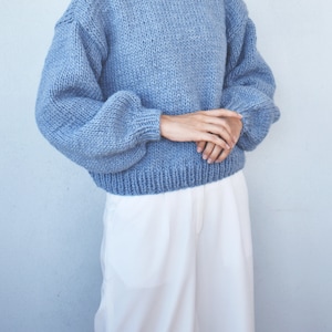 May include: A light blue knitted sweater with a round neckline and long, puffy sleeves.