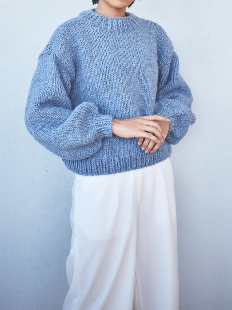 May include: A light blue knitted sweater with a round neckline and long, puffy sleeves.