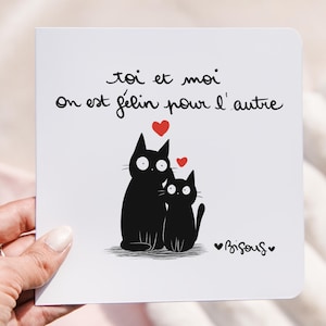 Peut inclure: Une carte blanche avec une illustration noire de deux chats et des coeurs rouges. La carte porte l'inscription "toi et moi on est félin pour l'autre" et "Bisous". Les chats sont assis ensemble.